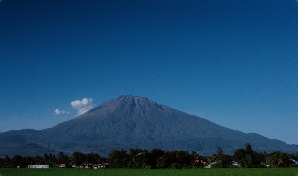 Scenic view of Mount Meru against a clear blue sky in Tanzania, showcasing its volcanic landscape.